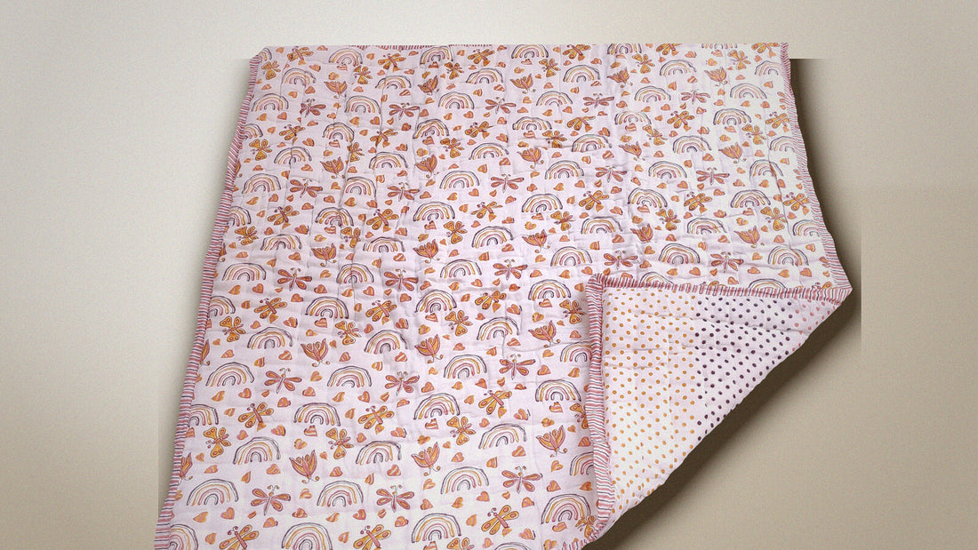 A hand block printed cotton baby quilt with a rainbow and butterfly print