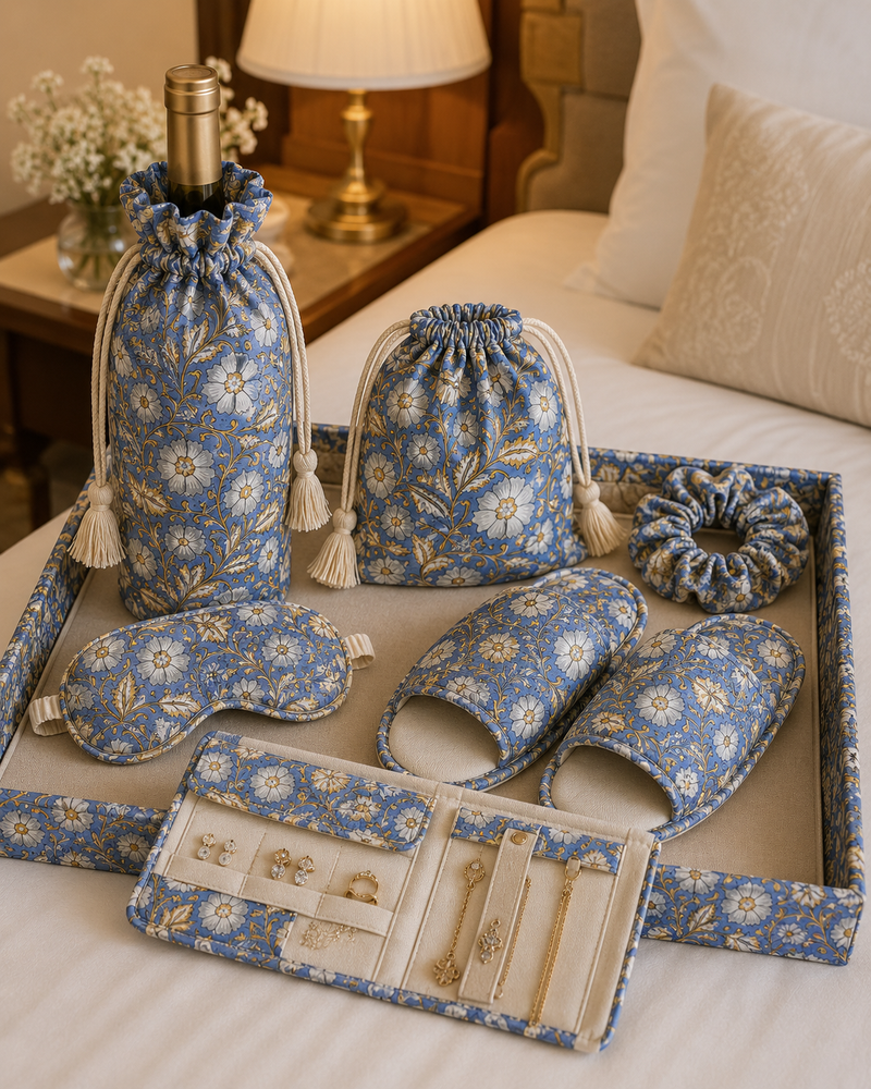 Hand block-printed welcome hamper — bottle bag, drawstring pouch, slippers, eye mask, scrunchie and jewellery case, styled on a hotel bed.